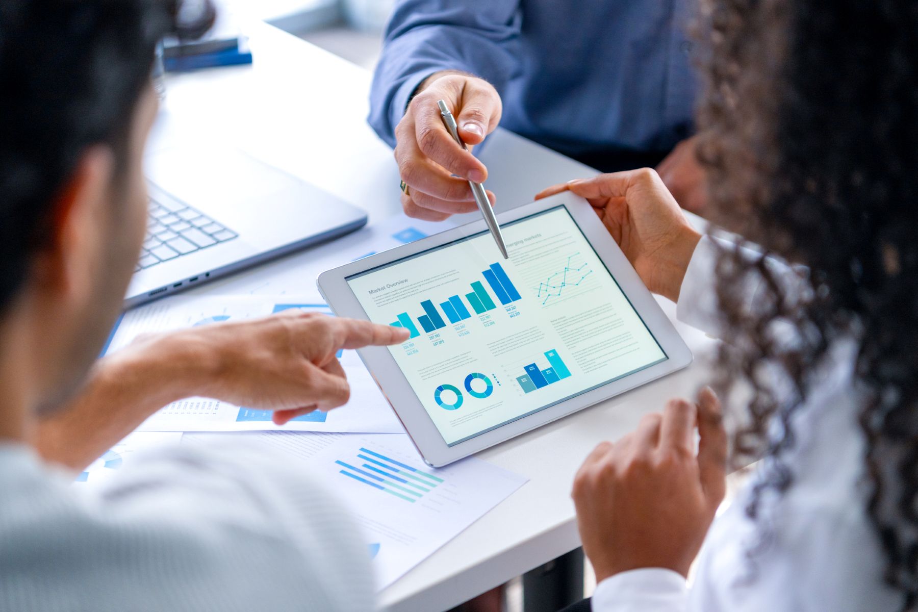 Primer plano de tres personas mirando datos financieros con gráficos y tablas