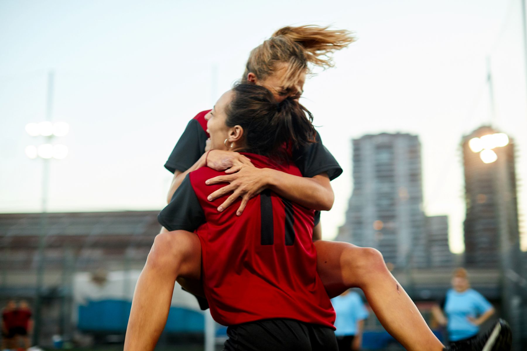Dos compañeras de equipo de fútbol se abrazan después de marcar un gol en la celebración.