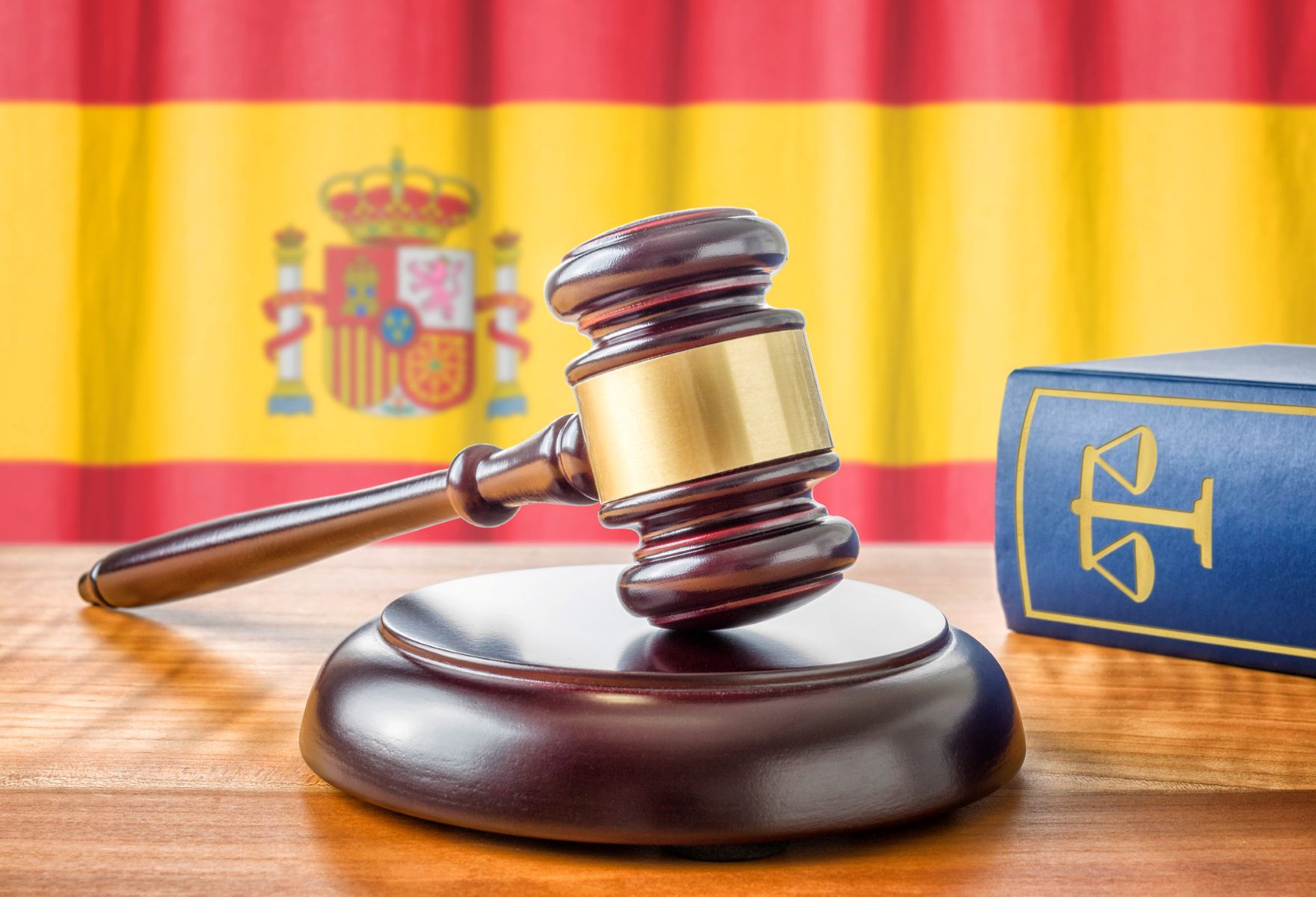 Mazo de juez y libro de derecho, con la bandera de España de fondo