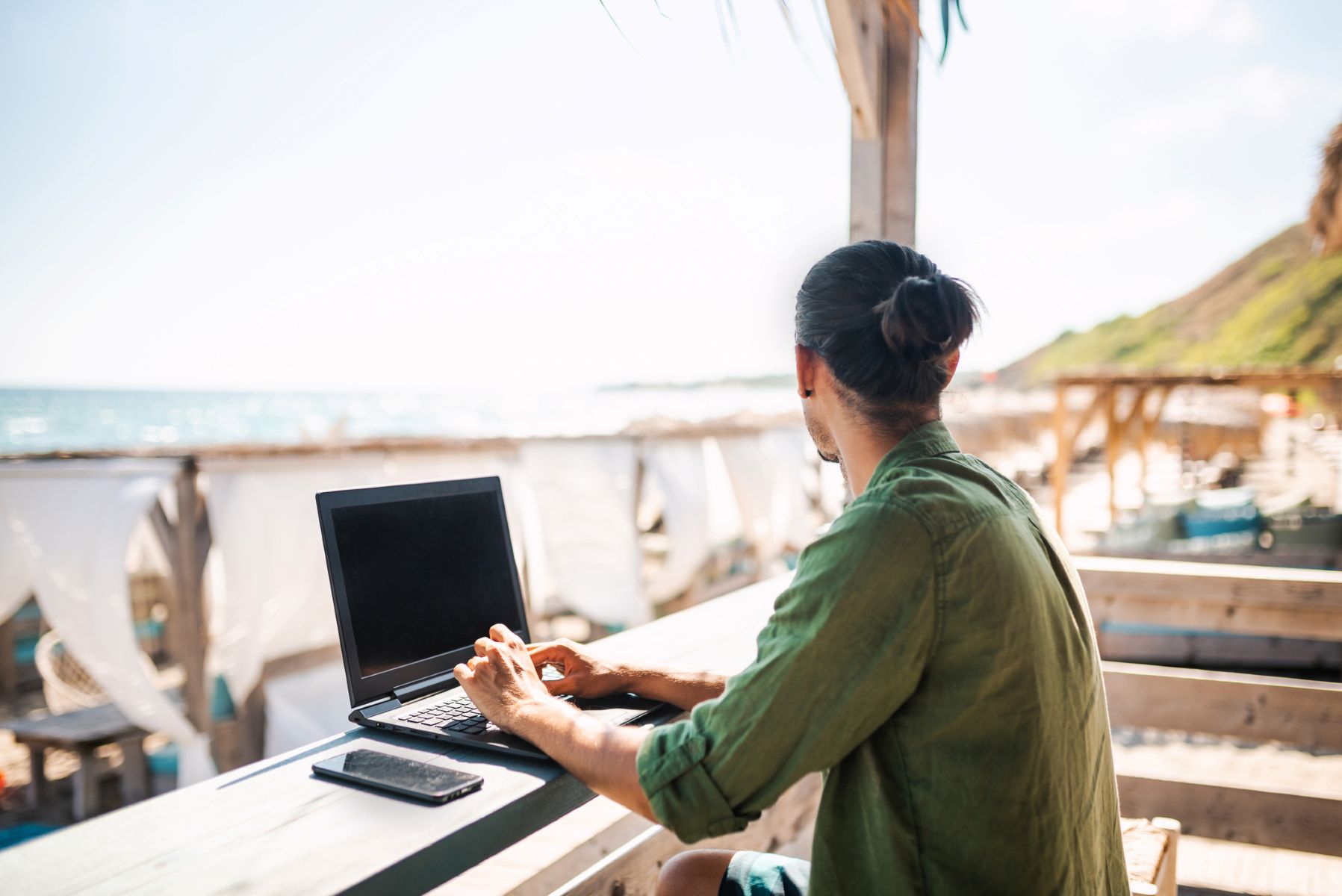 Trabajador autónomo teletrabajando con un ordenador portátil en un chiringuito de playa