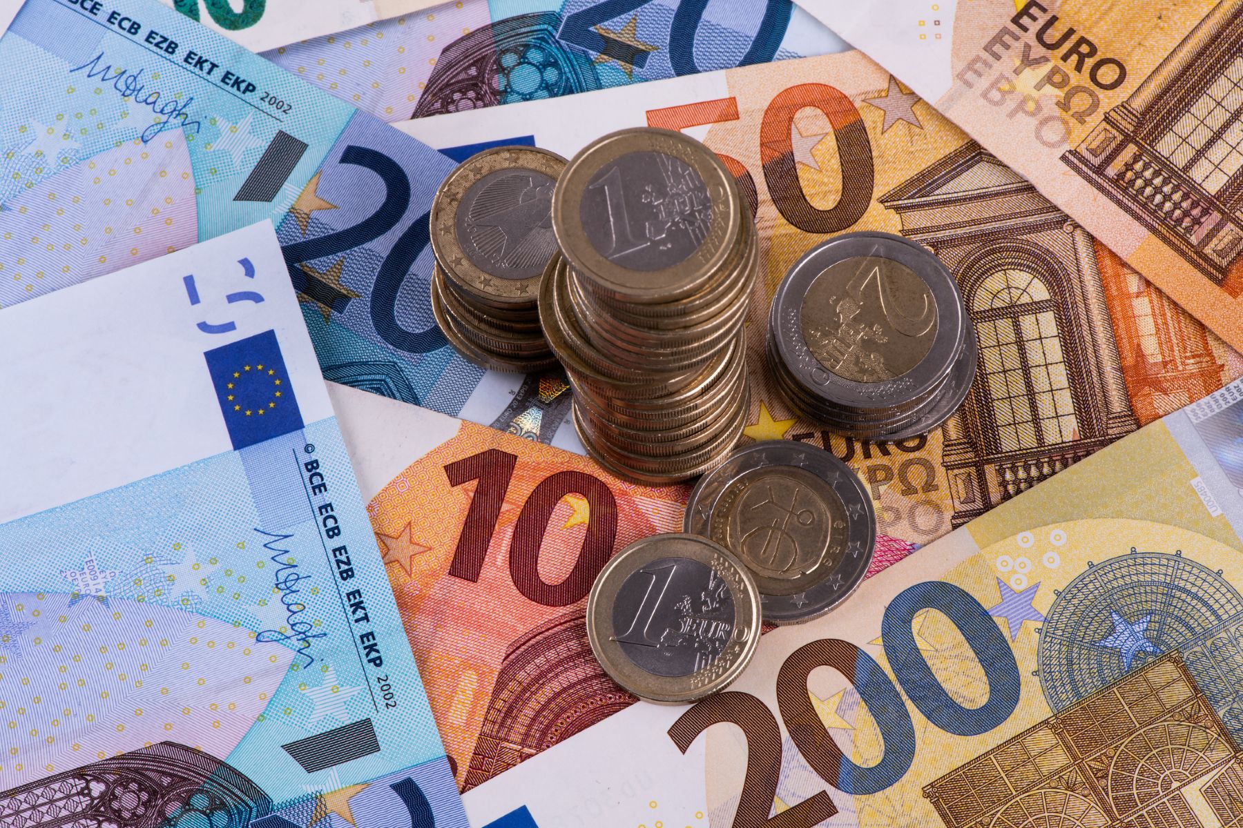 Pilas de monedas de 1 y 2 euros sobre tapiz de billetes de euro de diferente valor
