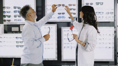 Dependienta en una cadena de ópticas enseñando gafas a un cliente