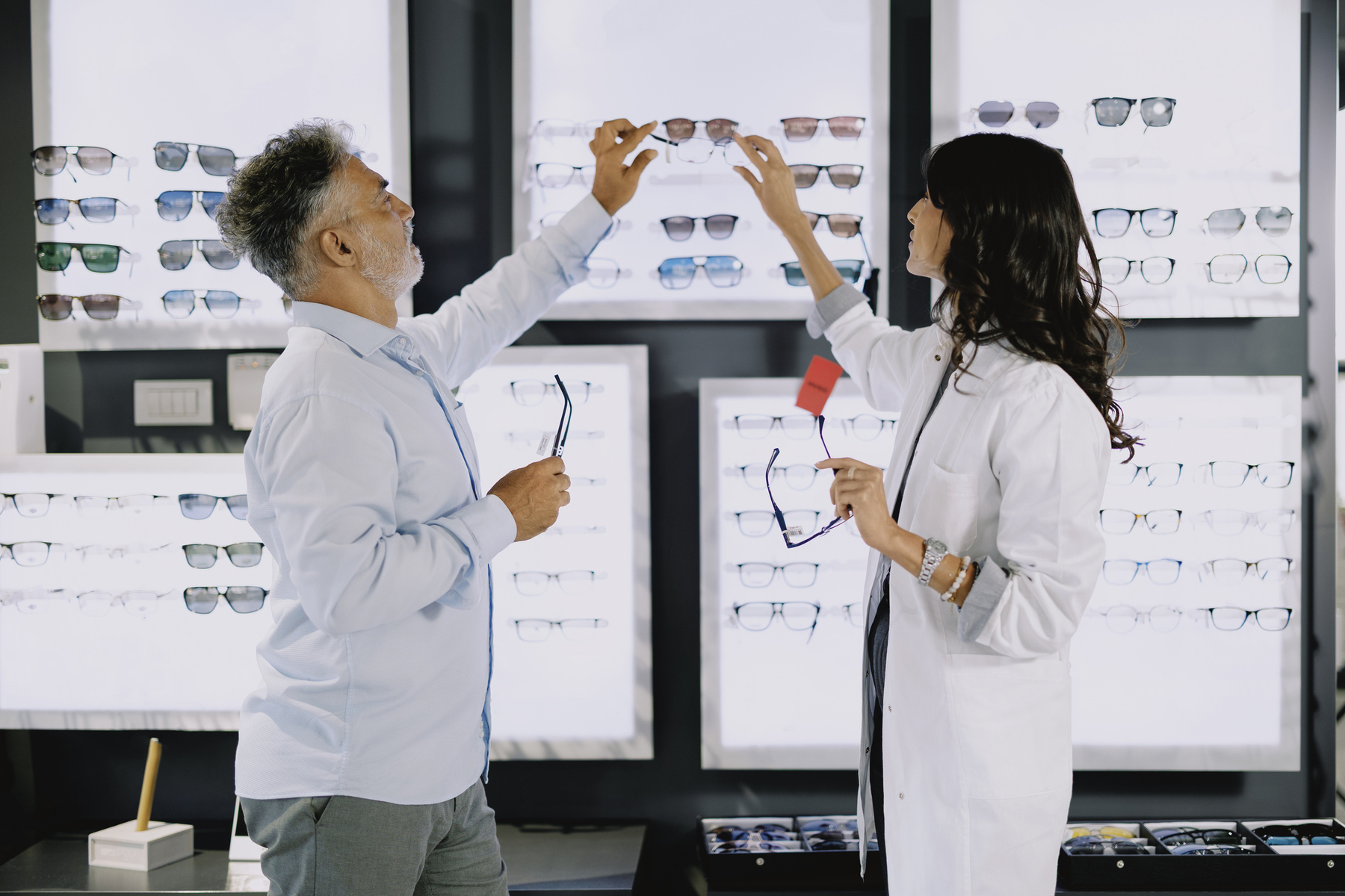 Dependienta en una cadena de ópticas enseñando gafas a un cliente