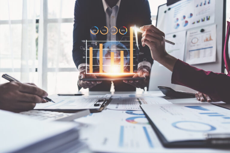 Primer plano de empleados trabajando sobre una mesa con gráficos en papel y gráficos digitales