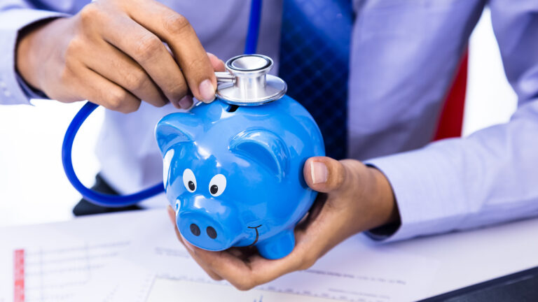 Empresario usando un estetoscopio con una hucha, como representación del concepto de salud financiera.