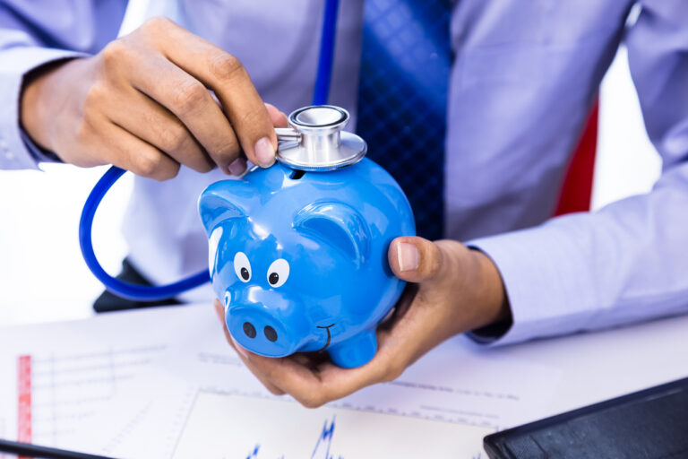 Empresario usando un estetoscopio con una hucha, como representación del concepto de salud financiera.