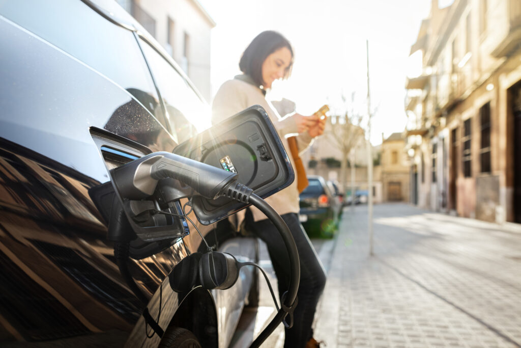 Vehículo eléctrico cargando mientras una chica mira el móvil. Foto: iStock