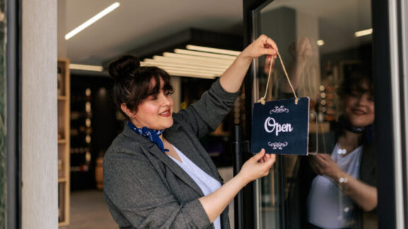 Propietaria de una pequeña empresa colgando cartel abierto en la puerta de la tienda