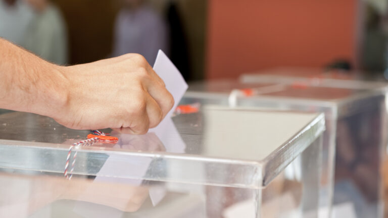Mano de hombre introduciendo un voto en la urna electoral