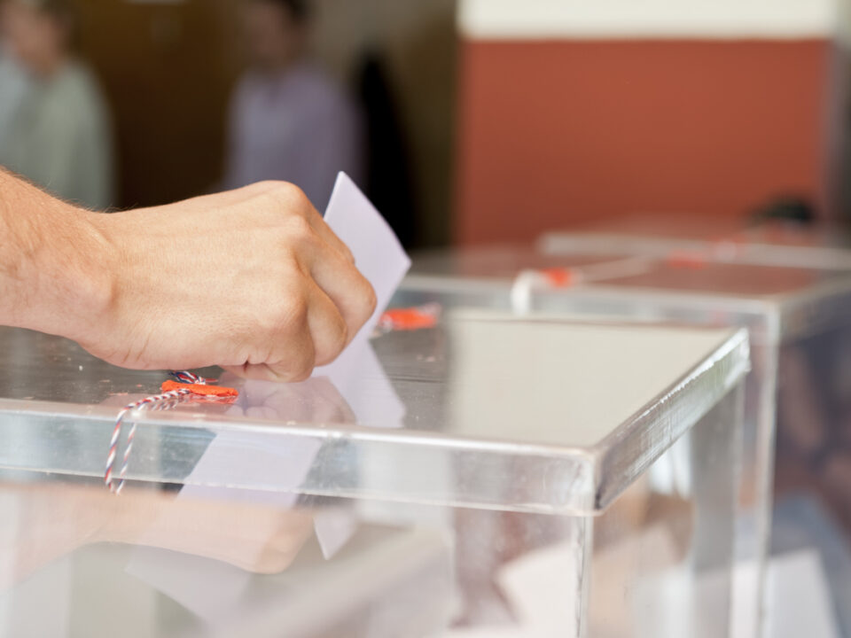 Mano de hombre introduciendo un voto en la urna electoral
