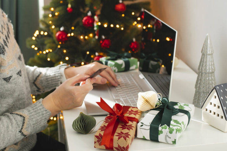 Mujer con tarjeta de pago en la mano frente a un portátil y con motivos navideños de fondo, a punto de realizar una compra en ecommerce