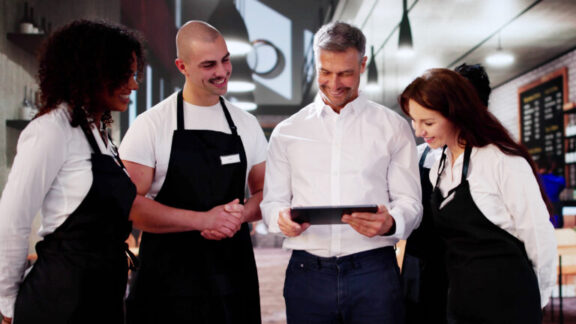 Un encargado revisa una tableta con su equipo de camareros en una cafetería