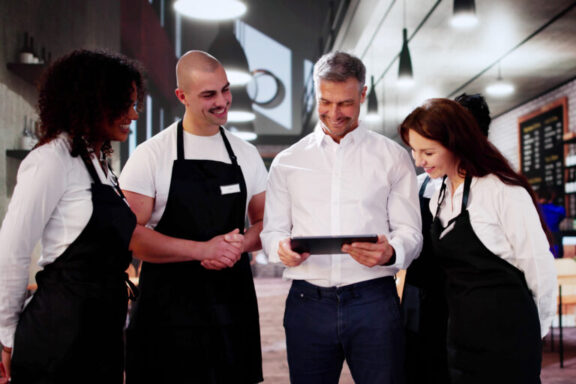 Un encargado revisa una tableta con su equipo de camareros en una cafetería