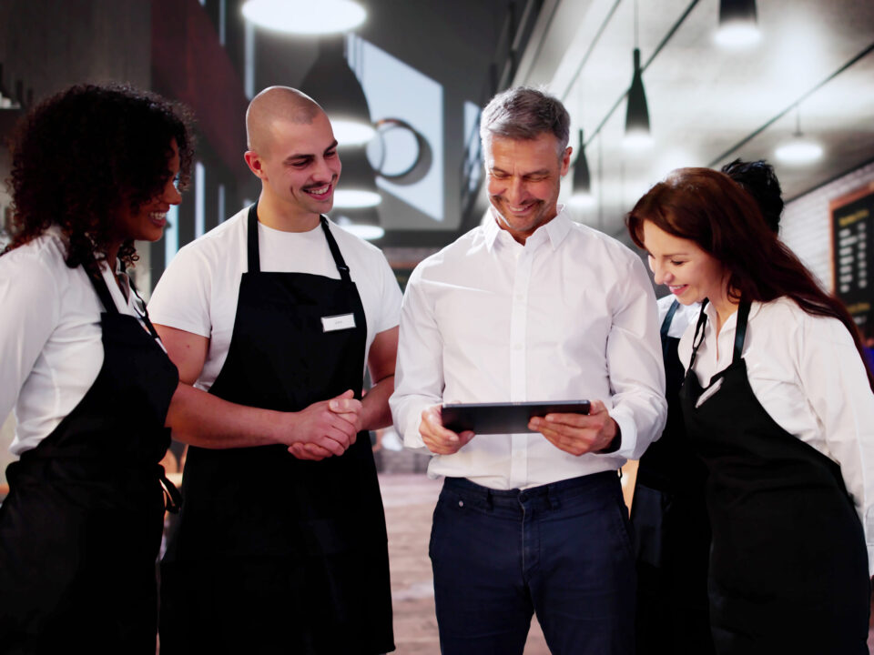 Un encargado revisa una tableta con su equipo de camareros en una cafetería