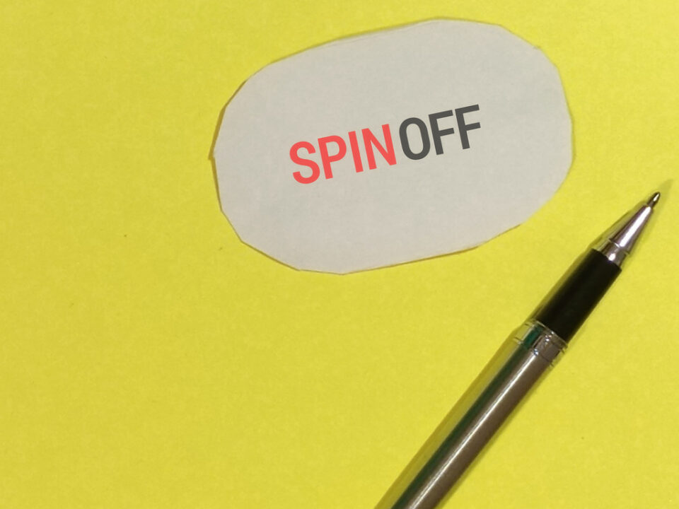 Palabra spin-off sobre fondo amarillo y con un bolígrafo al lado