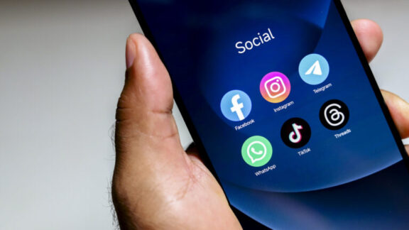 Hombre sujetando smartphone con iconos de apps de redes sociales en la pantalla.