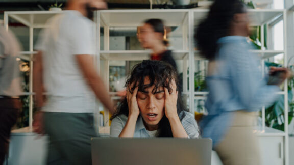 trabajadora estresada sosteniendo la cabeza en una oficina ocupada