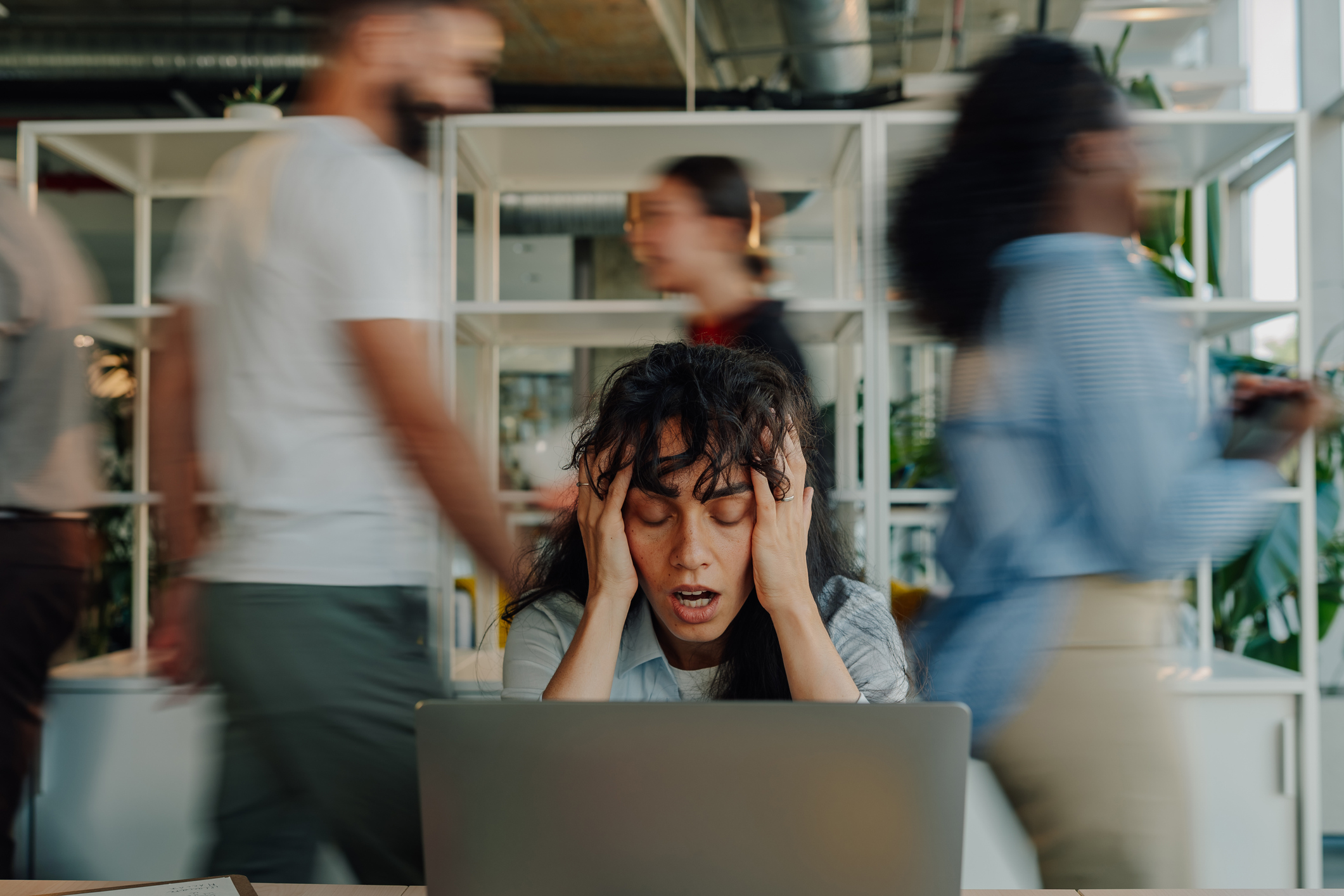trabajadora estresada sosteniendo la cabeza en una oficina ocupada